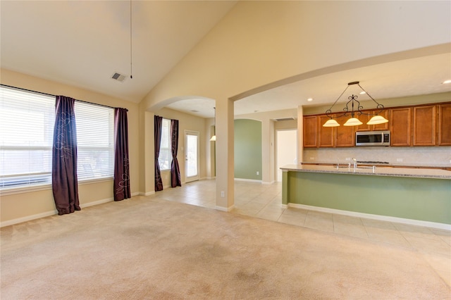 kitchen with high vaulted ceiling, backsplash, hanging light fixtures, light stone counters, and light carpet