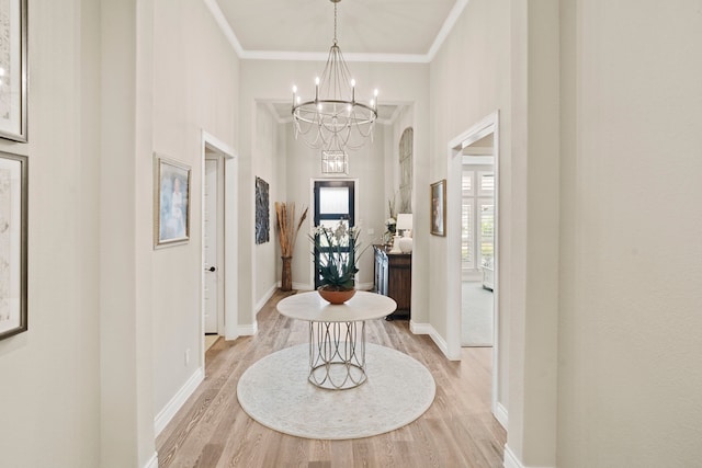 foyer entrance featuring crown molding, a towering ceiling, a chandelier, and light wood-type flooring