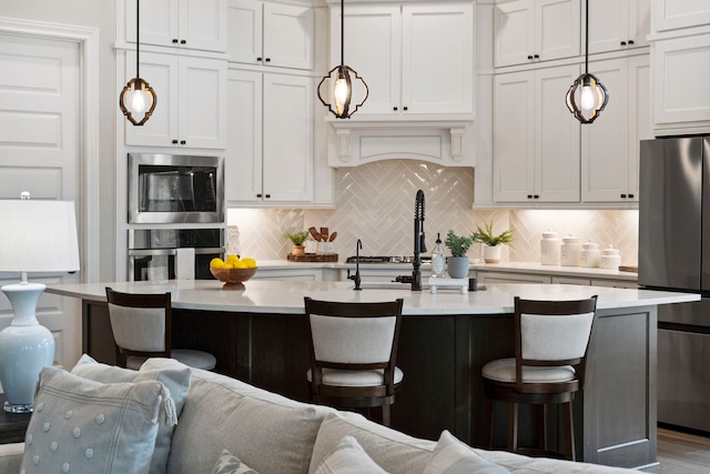 kitchen with pendant lighting, a breakfast bar area, appliances with stainless steel finishes, white cabinets, and a center island with sink