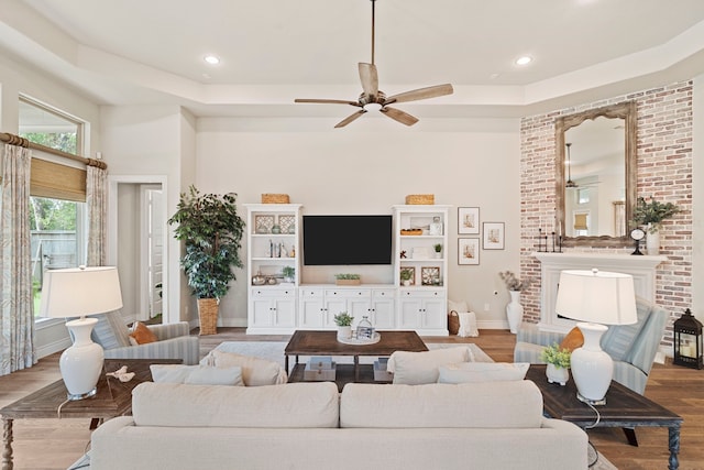 living room with a towering ceiling, a fireplace, ceiling fan, a tray ceiling, and light wood-type flooring