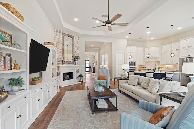 living room featuring dark hardwood / wood-style flooring, a tray ceiling, a large fireplace, and ceiling fan