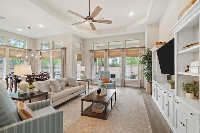 living room with a towering ceiling, a raised ceiling, ceiling fan with notable chandelier, and light wood-type flooring