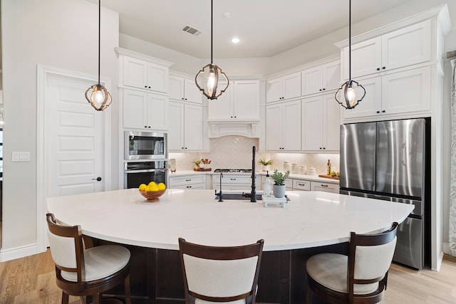 kitchen with white cabinetry, appliances with stainless steel finishes, a kitchen island with sink, and decorative backsplash