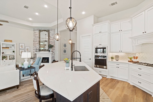 kitchen with sink, stainless steel appliances, an island with sink, white cabinets, and decorative light fixtures