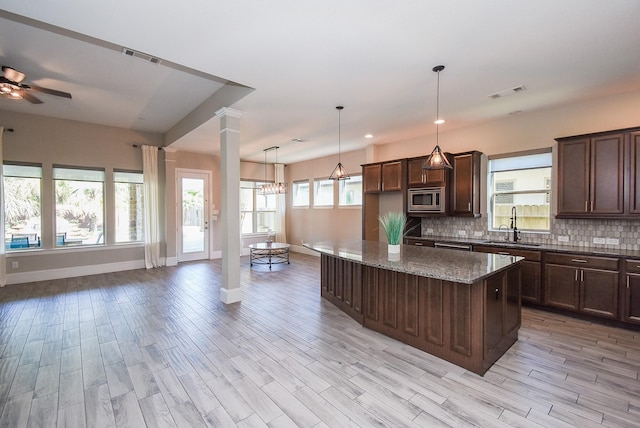 kitchen with pendant lighting, stone counters, stainless steel microwave, a kitchen island, and decorative backsplash