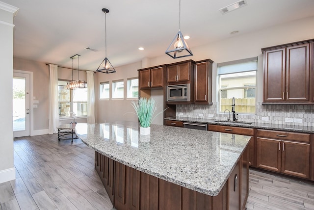 kitchen featuring a kitchen island, pendant lighting, sink, light stone counters, and stainless steel appliances