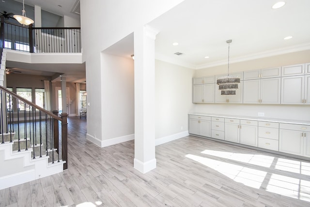 interior space with decorative light fixtures, a high ceiling, ceiling fan, crown molding, and light hardwood / wood-style flooring