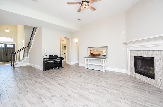 living room with ceiling fan, a fireplace, light hardwood / wood-style flooring, and a high ceiling