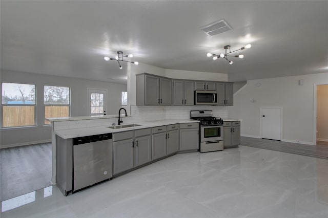 kitchen with appliances with stainless steel finishes, sink, gray cabinetry, decorative backsplash, and an inviting chandelier