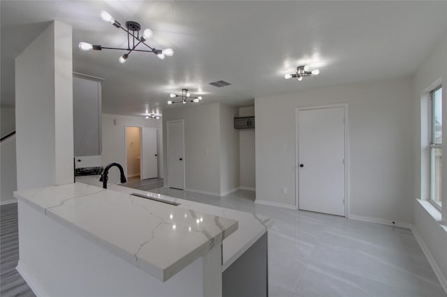 kitchen featuring light stone counters, an inviting chandelier, kitchen peninsula, and sink