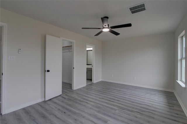 unfurnished bedroom with connected bathroom, a spacious closet, a closet, ceiling fan, and light hardwood / wood-style floors