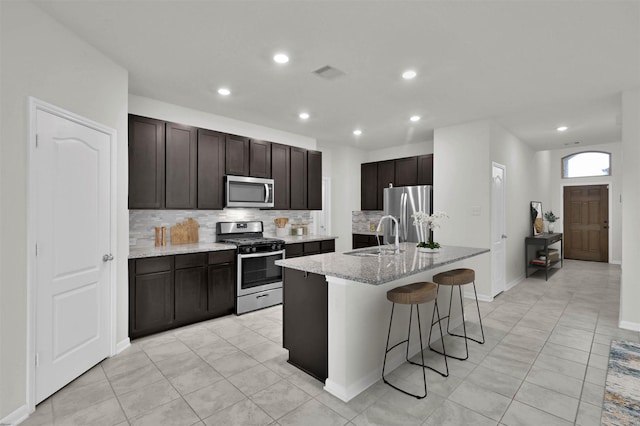 kitchen with dark brown cabinetry, sink, tasteful backsplash, a center island with sink, and appliances with stainless steel finishes