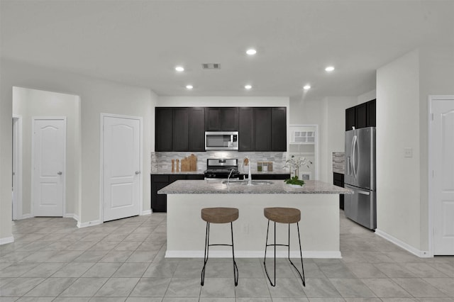 kitchen featuring sink, appliances with stainless steel finishes, a kitchen breakfast bar, a kitchen island with sink, and decorative backsplash