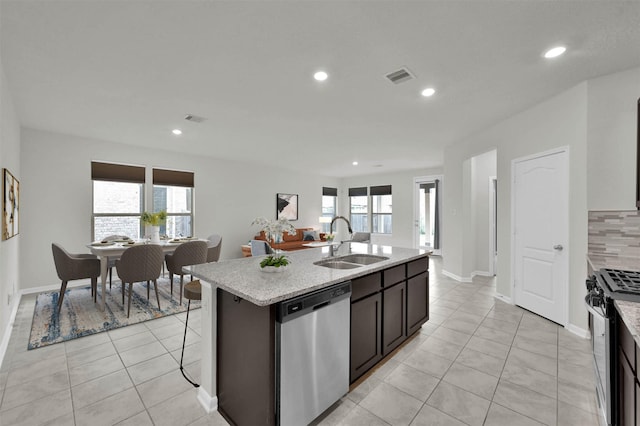 kitchen with sink, light tile patterned floors, appliances with stainless steel finishes, a kitchen island with sink, and dark brown cabinetry