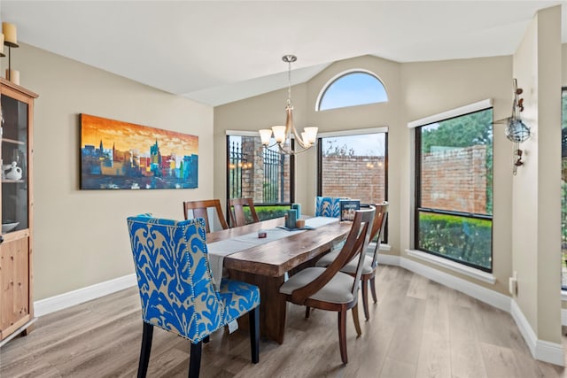 dining area with hardwood / wood-style flooring, plenty of natural light, vaulted ceiling, and a notable chandelier