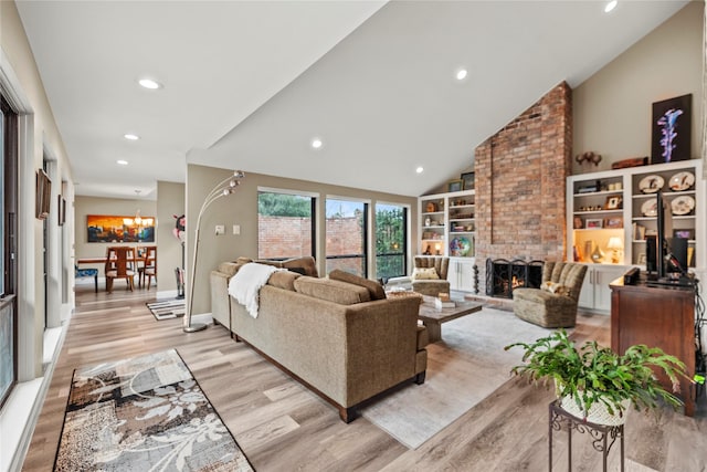 living room featuring built in features, high vaulted ceiling, a notable chandelier, a fireplace, and light wood-type flooring