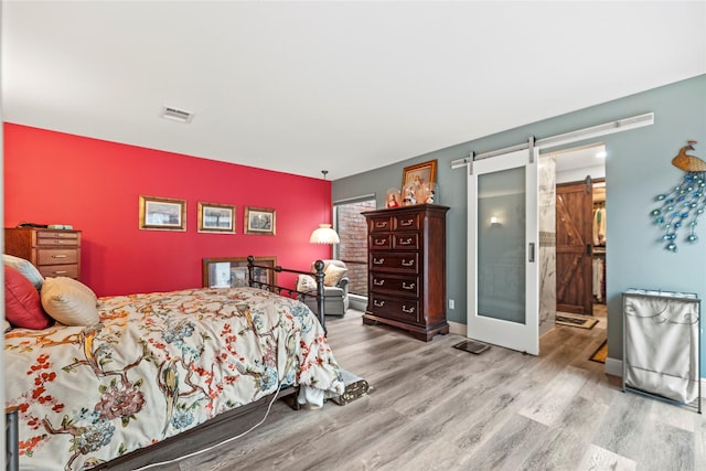 bedroom with a barn door and light wood-type flooring