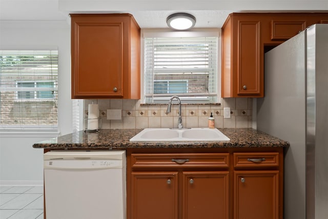 kitchen featuring tasteful backsplash, dishwasher, sink, dark stone countertops, and stainless steel fridge