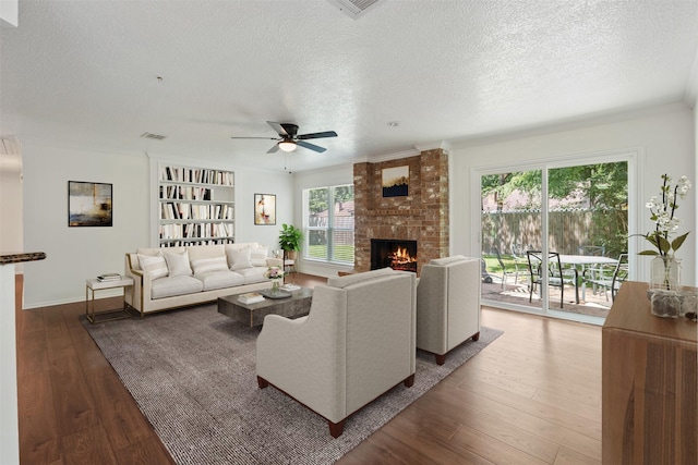 living room featuring hardwood / wood-style floors, ceiling fan, crown molding, a brick fireplace, and a textured ceiling