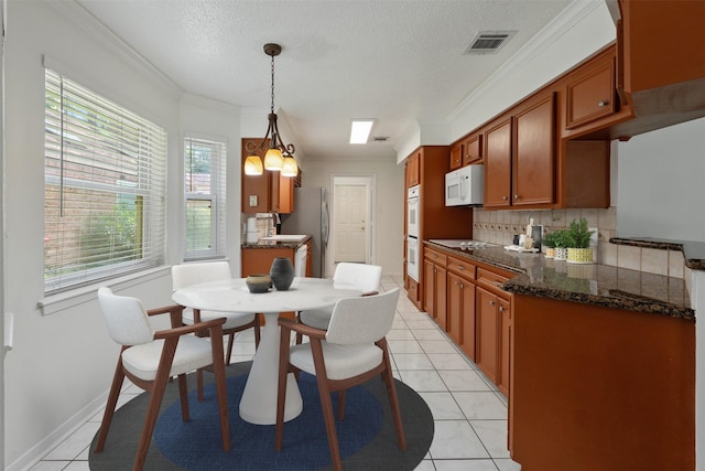 kitchen with hanging light fixtures, light tile patterned floors, ornamental molding, white appliances, and decorative backsplash