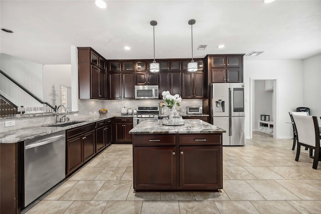 kitchen featuring light stone counters, dark brown cabinetry, a sink, appliances with stainless steel finishes, and tasteful backsplash