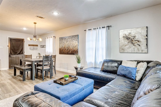 living room featuring a notable chandelier, a textured ceiling, and light wood-type flooring