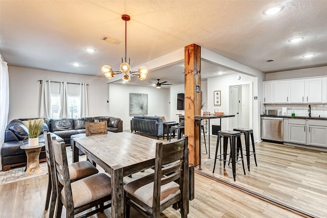 dining area with sink, ceiling fan with notable chandelier, light hardwood / wood-style floors, and a textured ceiling