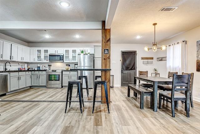 kitchen featuring tasteful backsplash, decorative light fixtures, light hardwood / wood-style flooring, and appliances with stainless steel finishes