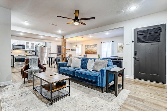 living room featuring ceiling fan with notable chandelier and light hardwood / wood-style flooring