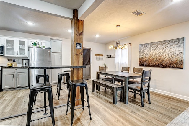 dining space with a textured ceiling, a chandelier, and light hardwood / wood-style flooring