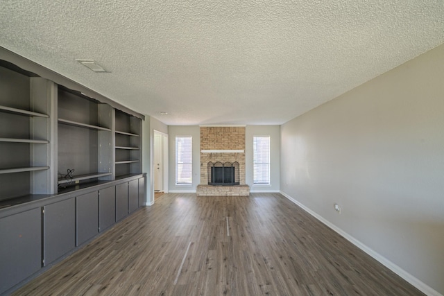 unfurnished living room with dark hardwood / wood-style flooring, a brick fireplace, and a textured ceiling