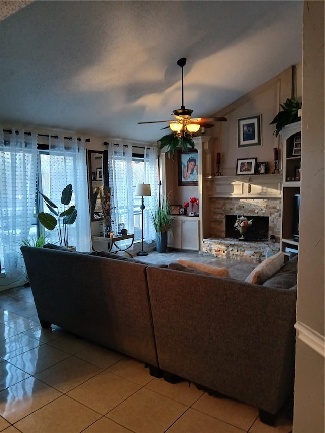 living room with ceiling fan, a stone fireplace, lofted ceiling, and tile patterned floors