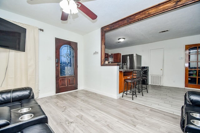 living room featuring ceiling fan, light hardwood / wood-style floors, and a textured ceiling