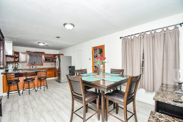 dining area with indoor wet bar, a textured ceiling, and light hardwood / wood-style floors