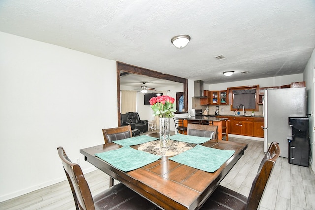 dining room with ceiling fan, sink, a textured ceiling, and light wood-type flooring