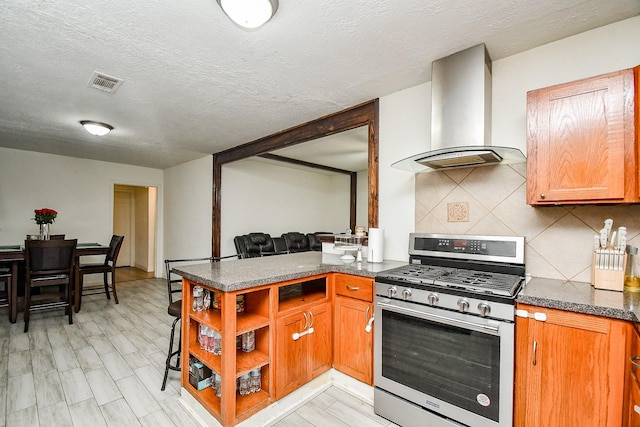 kitchen with wall chimney range hood, backsplash, gas stove, a textured ceiling, and kitchen peninsula