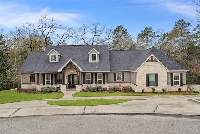 view of front of house with a chimney, a porch, a shingled roof, a front yard, and stone siding