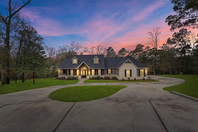 view of front of property featuring stone siding, curved driveway, and a front yard