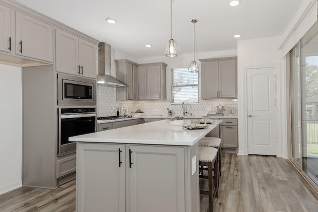 kitchen featuring gray cabinets, stainless steel appliances, wall chimney exhaust hood, and a kitchen island