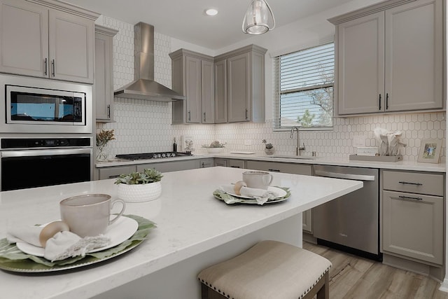 kitchen featuring wall chimney exhaust hood, sink, a breakfast bar area, decorative light fixtures, and stainless steel appliances