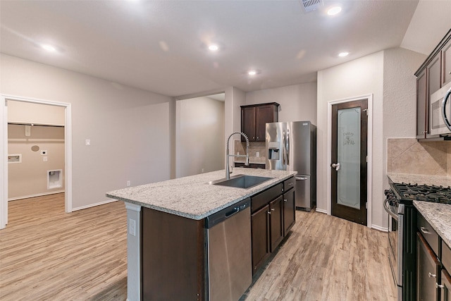 kitchen with dark brown cabinetry, appliances with stainless steel finishes, sink, and a center island with sink