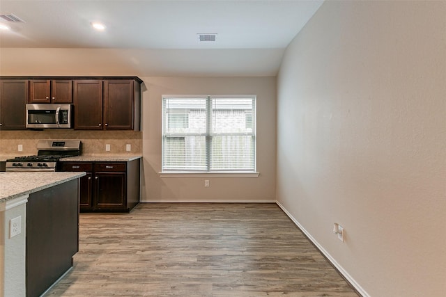 kitchen with dark brown cabinetry, light stone counters, light wood-type flooring, appliances with stainless steel finishes, and decorative backsplash