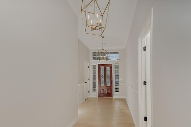 entryway featuring ornamental molding, a towering ceiling, an inviting chandelier, and light hardwood / wood-style flooring