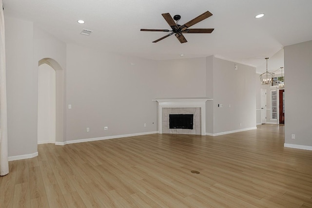 unfurnished living room with a fireplace, ceiling fan with notable chandelier, and light wood-type flooring