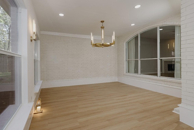 unfurnished dining area featuring brick wall, light hardwood / wood-style flooring, and a notable chandelier