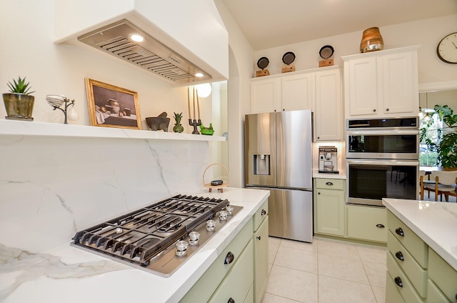 kitchen featuring light tile patterned flooring, tasteful backsplash, custom exhaust hood, green cabinetry, and stainless steel appliances