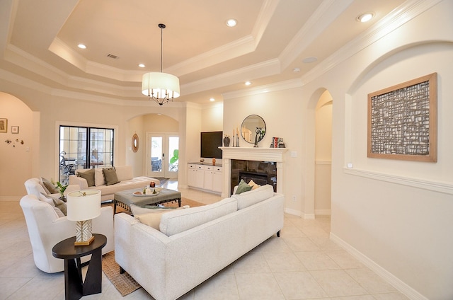 living room with crown molding, a tray ceiling, a tiled fireplace, and light tile patterned flooring