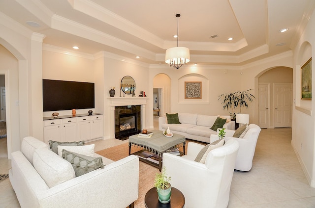 tiled living room featuring a tiled fireplace, ornamental molding, a raised ceiling, and a chandelier