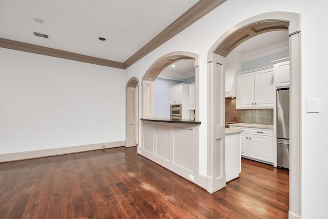 kitchen with white cabinetry, crown molding, appliances with stainless steel finishes, dark hardwood / wood-style floors, and backsplash