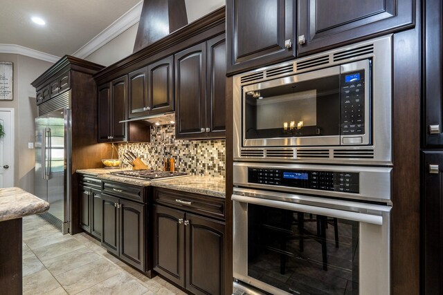 kitchen with dark brown cabinets, built in appliances, light stone counters, tasteful backsplash, and ornamental molding